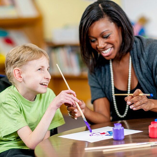 special needs student with a female teacher painting on a table