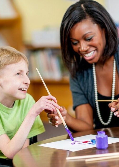 special needs student with a female teacher painting on a table